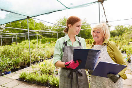 The gardener as boss and the young florist trainee work together in the garden centerの写真素材