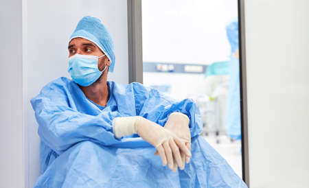 Surgeon sits tired and burned out in front of the intensive care unit due to overload from Covid-19の写真素材
