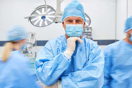 Portrait of surgeon in front of team in operating room with face mask and protective clothingの写真素材