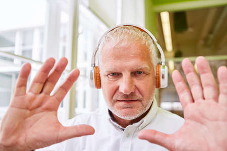 Senior business man with headphones gesturing during video conference in the officeの写真素材