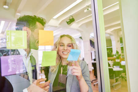 Young business people brainstorming in creative workshop with sticky notes on glassの写真素材