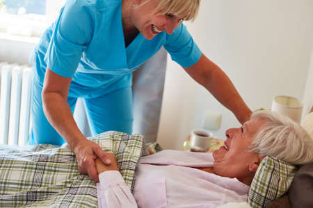 Nurse takes care of old woman as patient in bed at home or in old people's home