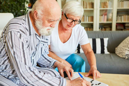 Geriatric nurse helps senior with dementia solve crossword puzzles as memory training at homeの写真素材