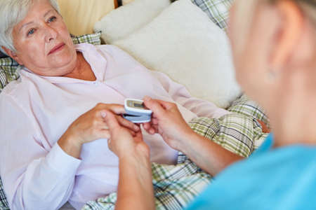 Geriatric nurse measures the pulse of a sick senior woman in bed in the retirement home with the...