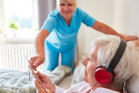 Geriatric nurse helps senior citizen in bed with headphones while listening to music streaming onlineの写真素材