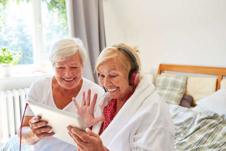 Senior woman happily waves at the webcam during a video call with family in the retirement home or at homeの写真素材