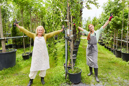 Two women gardeners team cheering with arms outstretched in a nursery