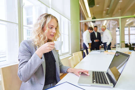 Young businesswoman at laptop computer in office drinking a cup of coffee