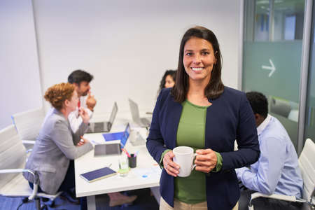 Happy business woman with a cup of coffee in a meeting in front of her team