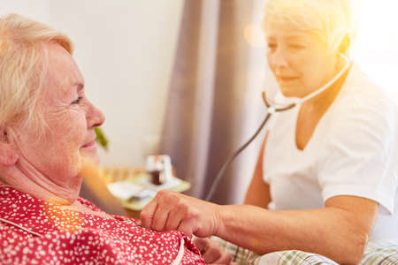 Elderly nurse listening to lungs with stethoscope at senior citizen's homeの写真素材
