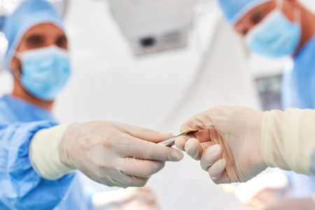 Resident doctor with disposable gloves gives the scalpel to colleagues during an emergency operationの写真素材