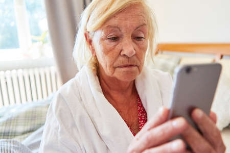 Lonely and sad elderly woman in the nursing home video chat with the family on the smartphoneの写真素材