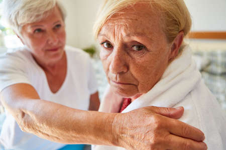 Old woman as a depressed patient in a nursing home is comforted by a geriatric nurse