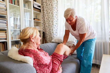 Physiotherapist treating a senior citizen's knee on the sofa in home careの写真素材