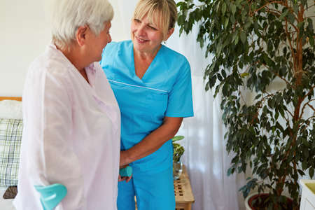 Geriatric nurse helps senior citizen with crutches when walking in geriatric care or in the rehab clinicの写真素材