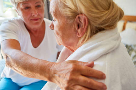 A woman from the nursing service looks after a demented elderly woman in a bathrobe at home
