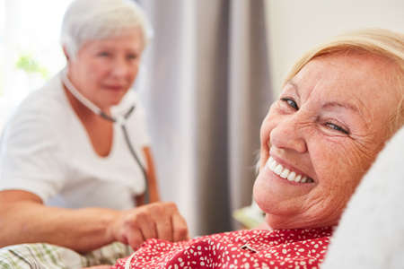 Happy elderly woman as a patient in bed is examined by a doctor with a stethoscopeの写真素材