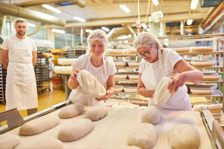 Baker women team baking a loaf of bread in a large bakery or bakery