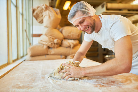 Young baker kneading dough with flour in preparation for baking bread in bakeryの写真素材