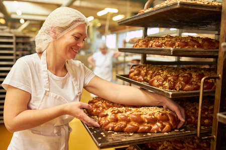 Female baker with fresh yeast plaited bread with almonds straight from the oven in a large bakery