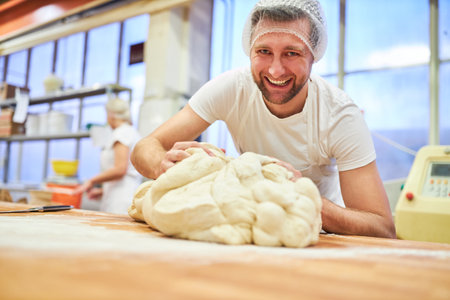 Young apprentice baker has fun kneading dough in preparation for baking in bakeryの写真素材