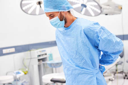 Surgeon wearing a face mask while putting on a gown as preparation for the operation in the...
