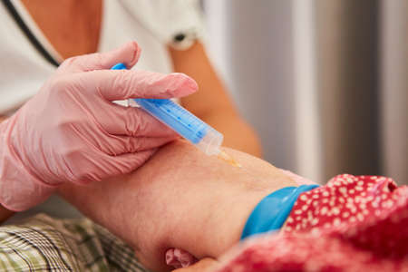 Doctor gives senior citizen an injection of vitamins or an injection against pain in the forearmの写真素材