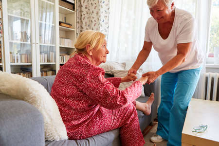 Nursing woman helping old woman get up from sofa in home careの写真素材