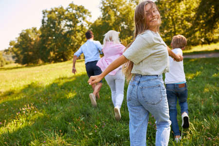 Teenager running across a green meadow in summer together with parents and brother