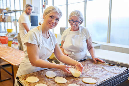 Young woman baker apprentice in apprenticeship baking with instruction in bakery