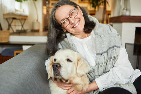 Senior man as a happy pensioner cuddling with her retriever dog on the sofa at home