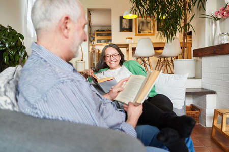Happy senior couple as pensioners reading a book for relaxation in the living room at home