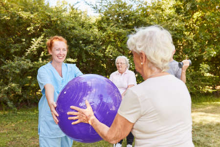 Physiotherapist and seniors do an exercise with the exercise ball in the garden of the rehabilitation clinicの写真素材