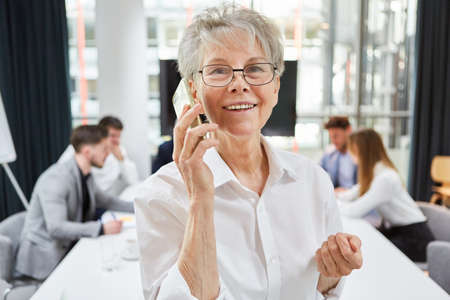 Smiling senior business woman talking on smartphone in meeting in conference roomの写真素材