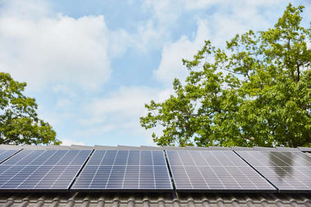 Modern solar system on roof of family house in front of a green tree and a blue sky
