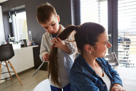 Little boy combing his mother's ponytail while playing hairdresser in the living roomの写真素材