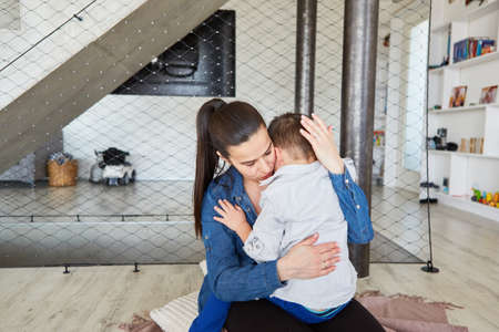 Mother lovingly hugs her sad son and comforts him at home in the living roomの写真素材