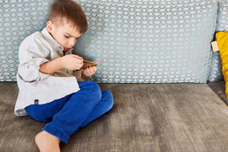 Little boy reads a text message on his smartphone or on social media with concentrationの写真素材
