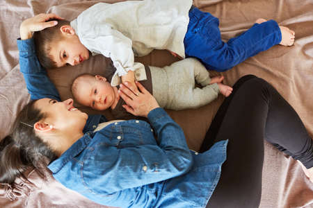 Happy mother cuddling with baby and big brother on a blanket in the living roomの写真素材