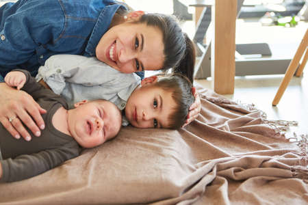 Happy mother cuddling with son and newborn baby on sofa in living roomの写真素材
