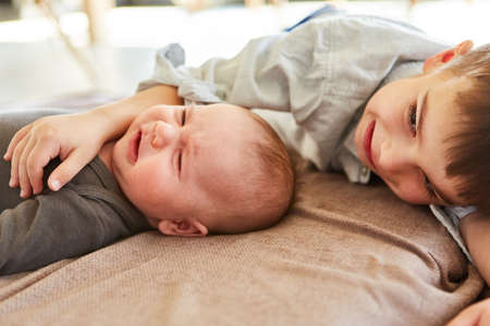 Boy as big brother comforts crying baby while cuddling together in living room