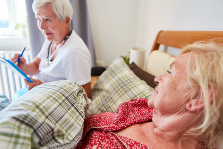 Elderly as a patient in bed and a doctor with patient files during a home visit to the nursing homeの写真素材