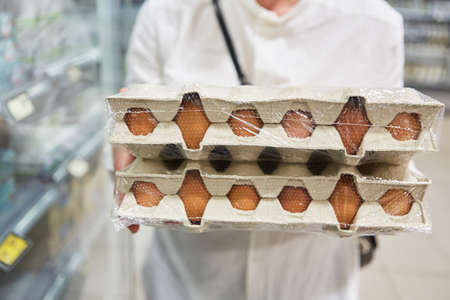 Customer carries stack of organic egg cartons while shopping in supermarketの写真素材