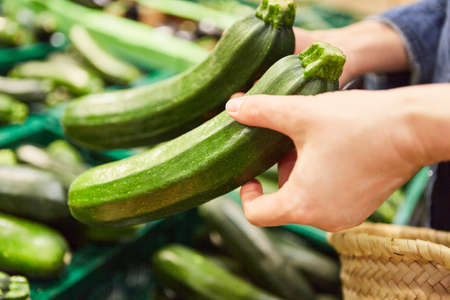 Hands of a customer with two zucchini while shopping in the market or supermarketの写真素材