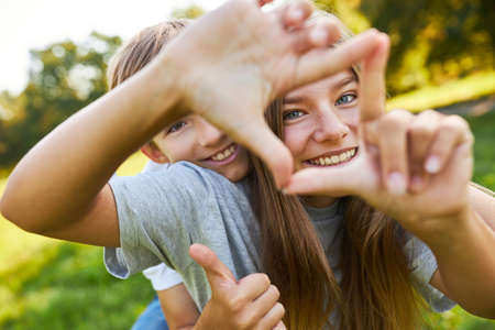 Brother and sister form a square with their hands while playing in nature