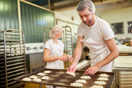 Young man as a baker's apprentice baking yeast plaits in a large bakery
