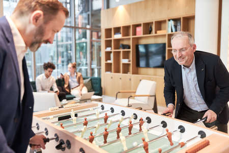 Business people play foosball at the foosball table during a break in the office lounge