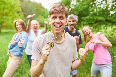 Happy man proudly shows his medal in front of cheering team after a win