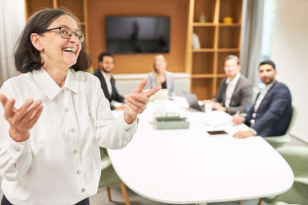 Dynamic business woman as motivational speaker in coaching workshop with team in backgroundの写真素材