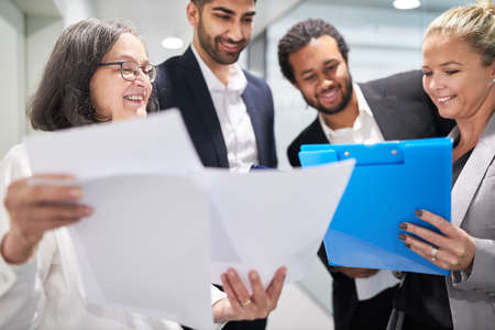 Happy business team on the hallway of the office looking at contract or documents together